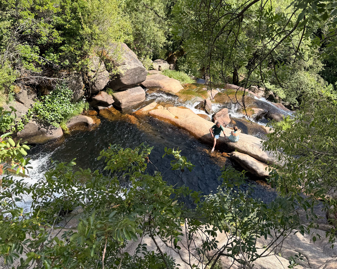 Two people sitting on rocks beside forest waterfall