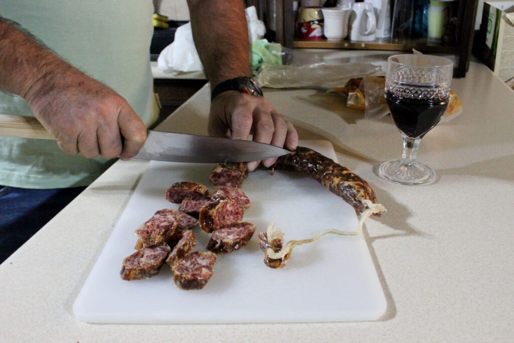 Slicing cured sausage next to a glass of red wine