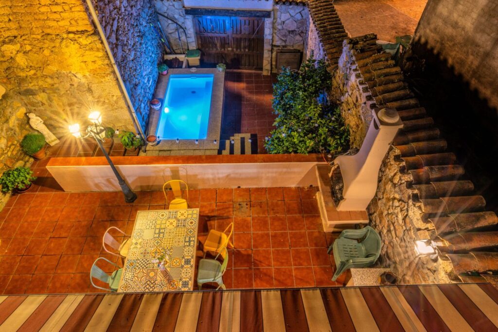 The patio of the house at night, with the small pool lit up, seen from above